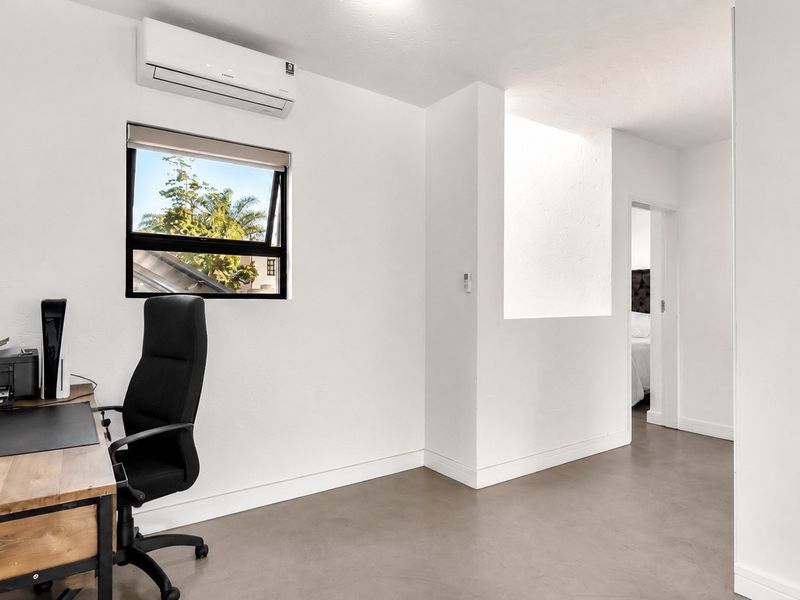 A bright, modern home office featuring polished concrete floors, a wall-mounted air conditioning unit, and a window with natural light.