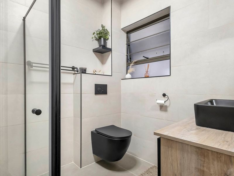 Modern bathroom featuring a wall-mounted toilet, glass shower enclosure with black framing, and a contemporary vanity with a vessel sink.