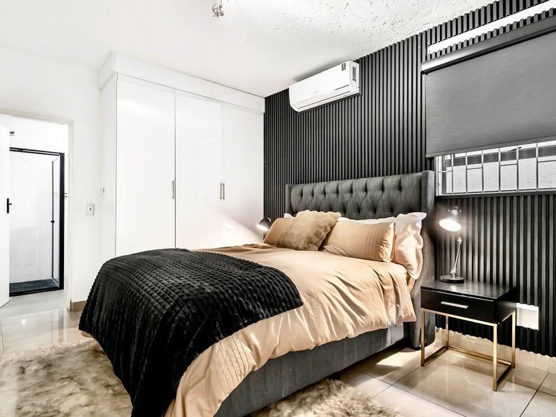 Modern bedroom featuring a stylish slatted accent wall, built-in cupboards, tiled flooring, and a wall-mounted air conditioning unit.