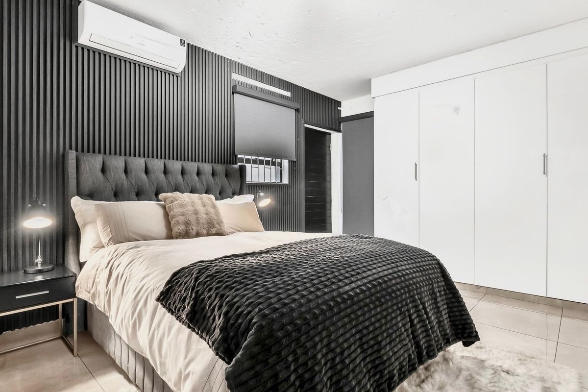 Modern bedroom featuring sleek slatted wall paneling, a built-in wardrobe, tiled flooring, and a wall-mounted split-system air conditioner.