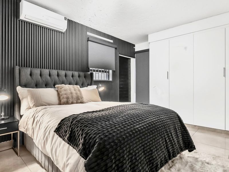 Modern bedroom featuring sleek slatted wall paneling, a built-in wardrobe, tiled flooring, and a wall-mounted split-system air conditioner.