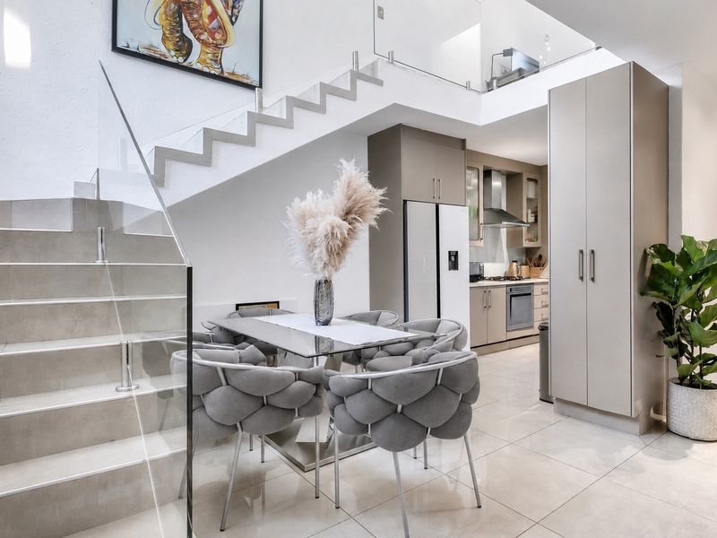 Modern open-plan living area featuring a sleek glass-railed staircase, tiled flooring, and a contemporary kitchen with integrated cabinetry and built-in appliances.