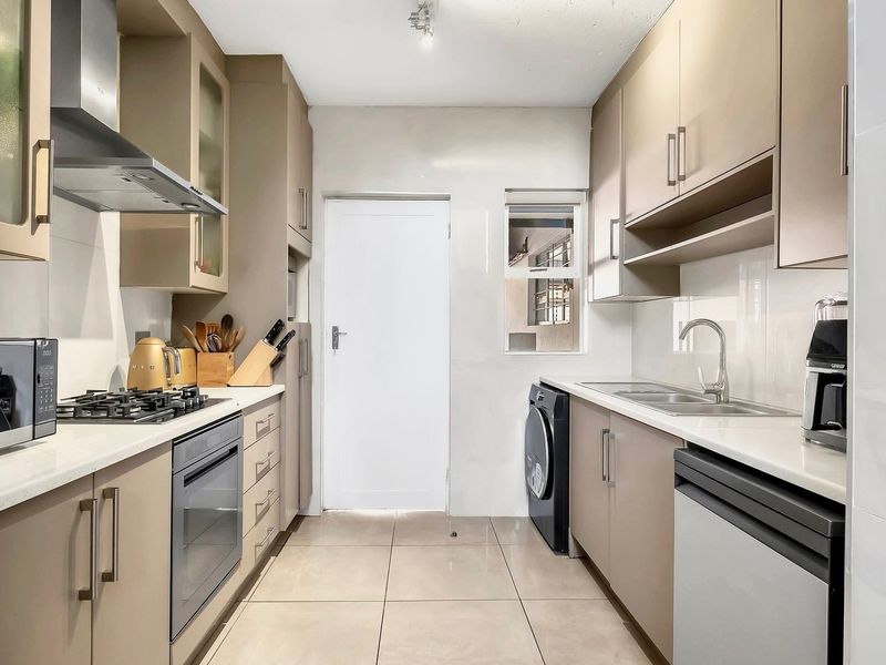 Modern galley-style kitchen featuring neutral cabinetry, stone countertops, gas hob, built-in oven, and integrated sink with tiled flooring.