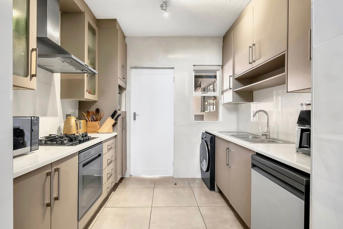 Modern galley-style kitchen featuring neutral cabinetry, stone countertops, gas hob, built-in oven, and integrated sink with tiled flooring.
