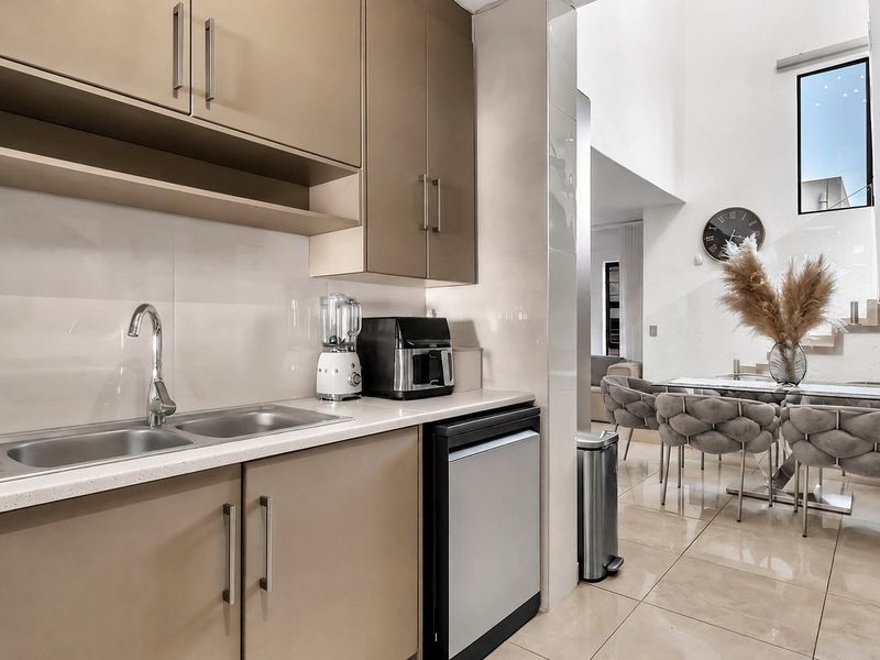 A modern scullery area featuring sleek built-in cabinetry, stone countertops, and a stainless steel sink, seamlessly connected to the adjacent dining space.