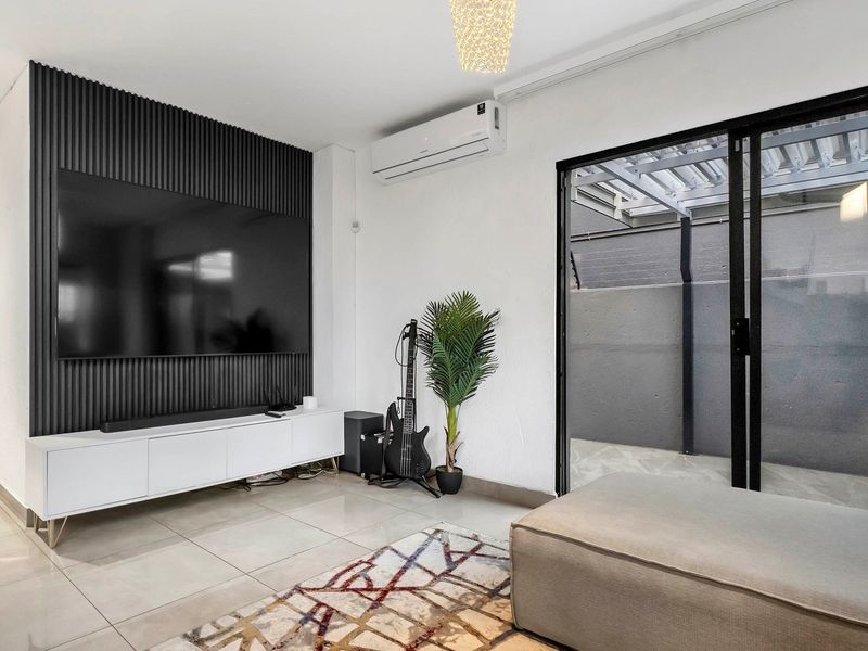 Modern living room featuring a stylish slatted feature wall, split-system air conditioning, large format floor tiles, and direct access to an outdoor patio area.