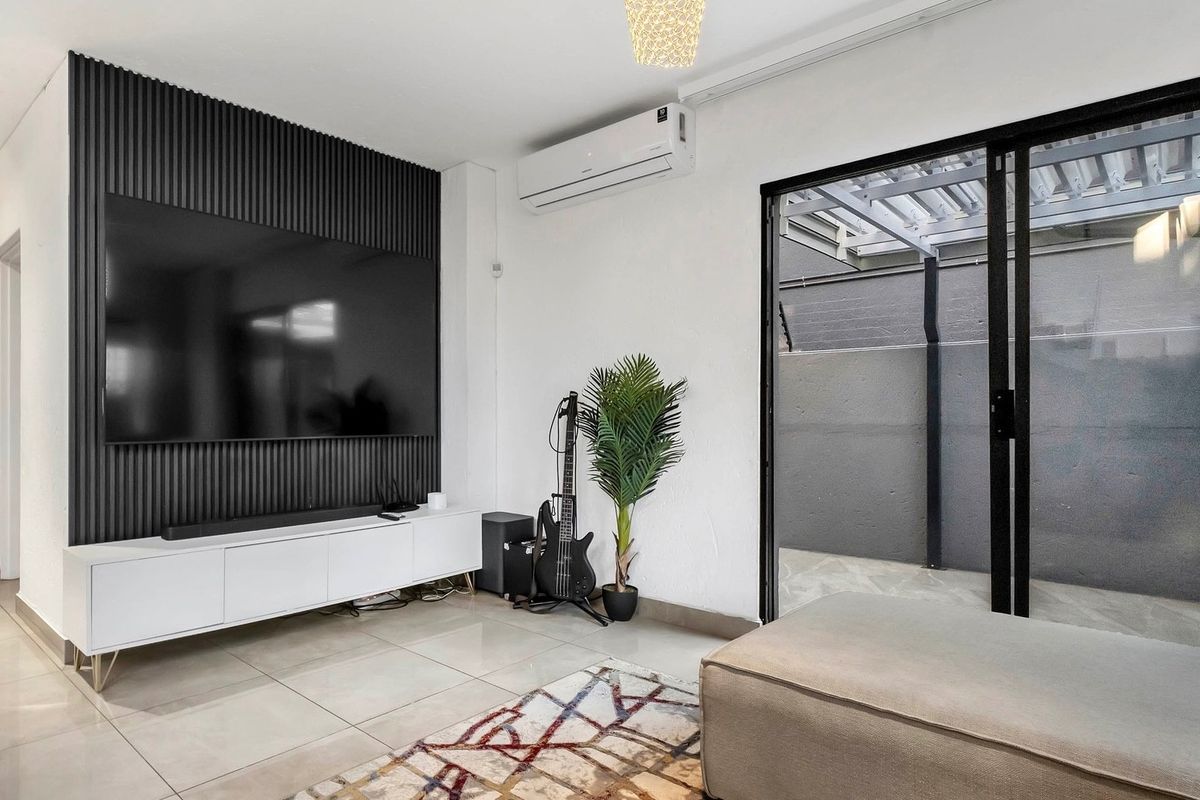 Modern living room featuring a stylish slatted feature wall, split-system air conditioning, large format floor tiles, and direct access to an outdoor patio area.