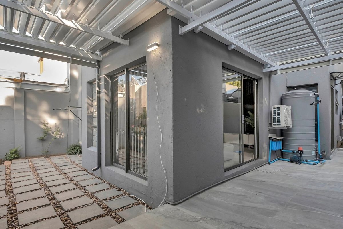 A modern rear courtyard featuring a paved patio, aluminium sliding doors, a pergola, and integrated water storage and filtration systems.
