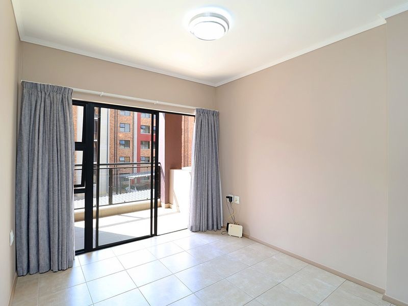 A bright, empty bedroom featuring neutral tiled flooring and a large sliding glass door that opens onto a private balcony.