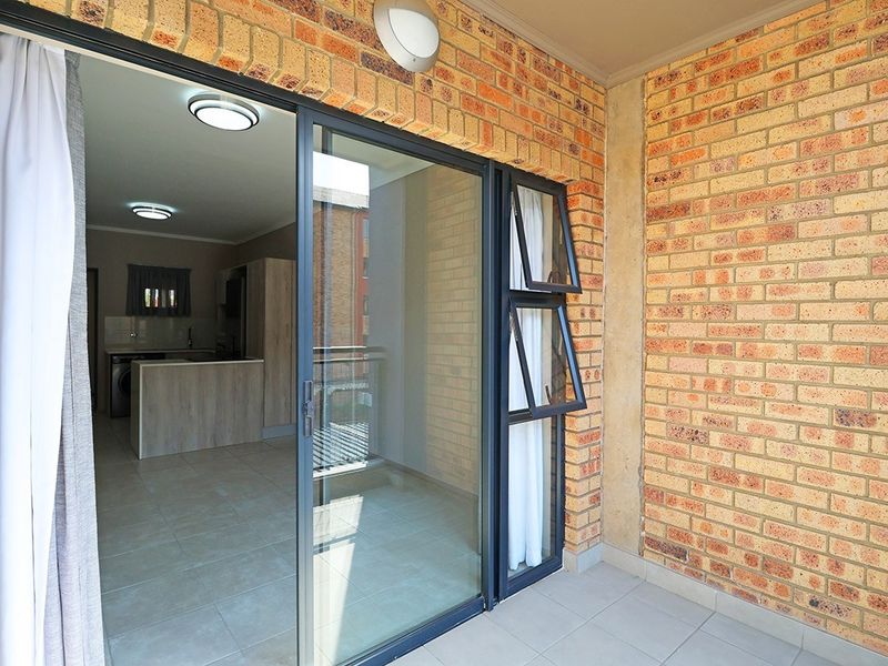 A covered balcony featuring exposed brick walls, tiled flooring, and a large sliding glass door providing access to the interior living space.