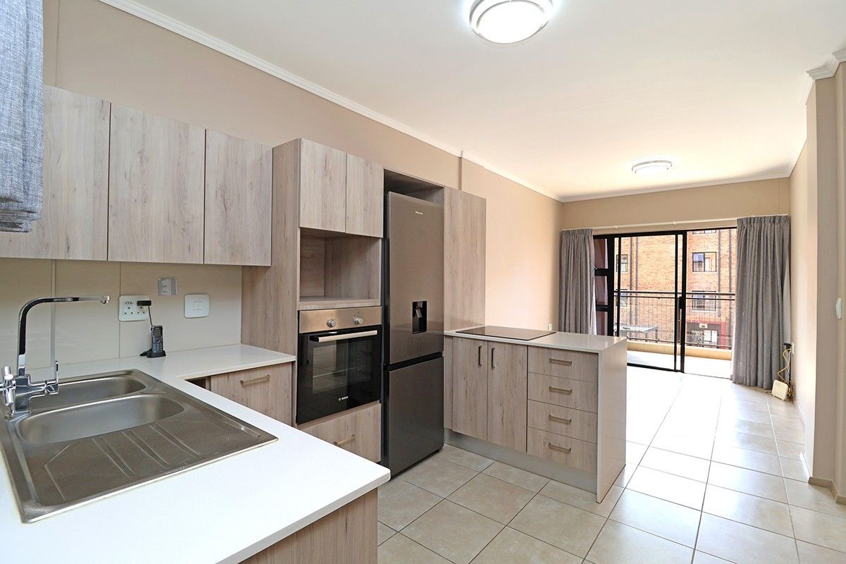 Modern open-plan kitchen featuring light wood-grain cabinetry, built-in oven, cooktop, and tiled flooring, leading to a balcony with sliding glass doors.