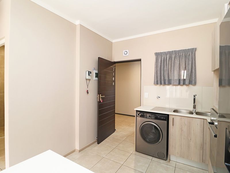 A clean and functional laundry area featuring built-in cabinetry, a stainless steel sink, and tiled flooring, providing efficient utility space.