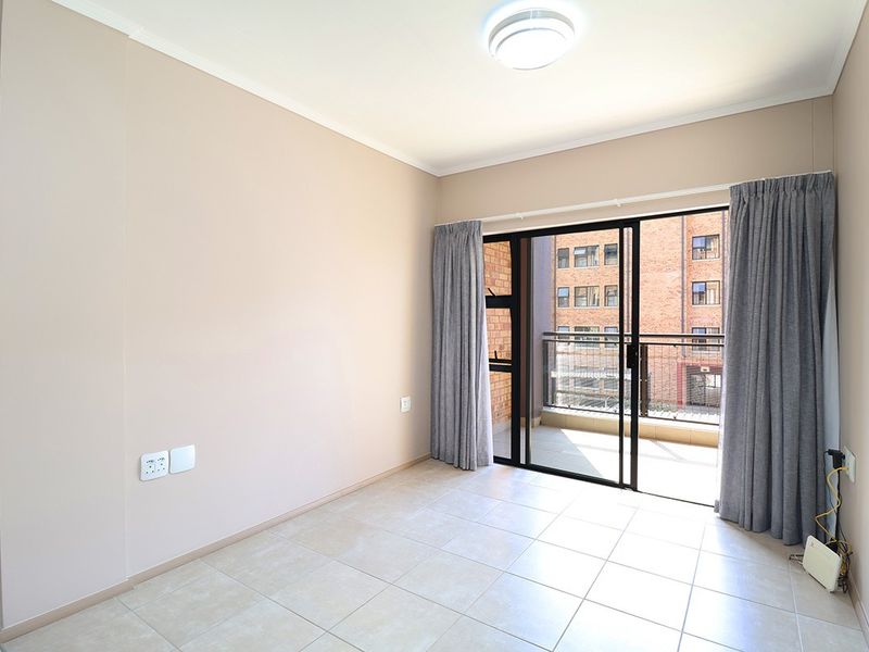 A bright, empty bedroom featuring neutral tiled flooring, a ceiling light fixture, and a sliding glass door providing direct access to a private balcony.