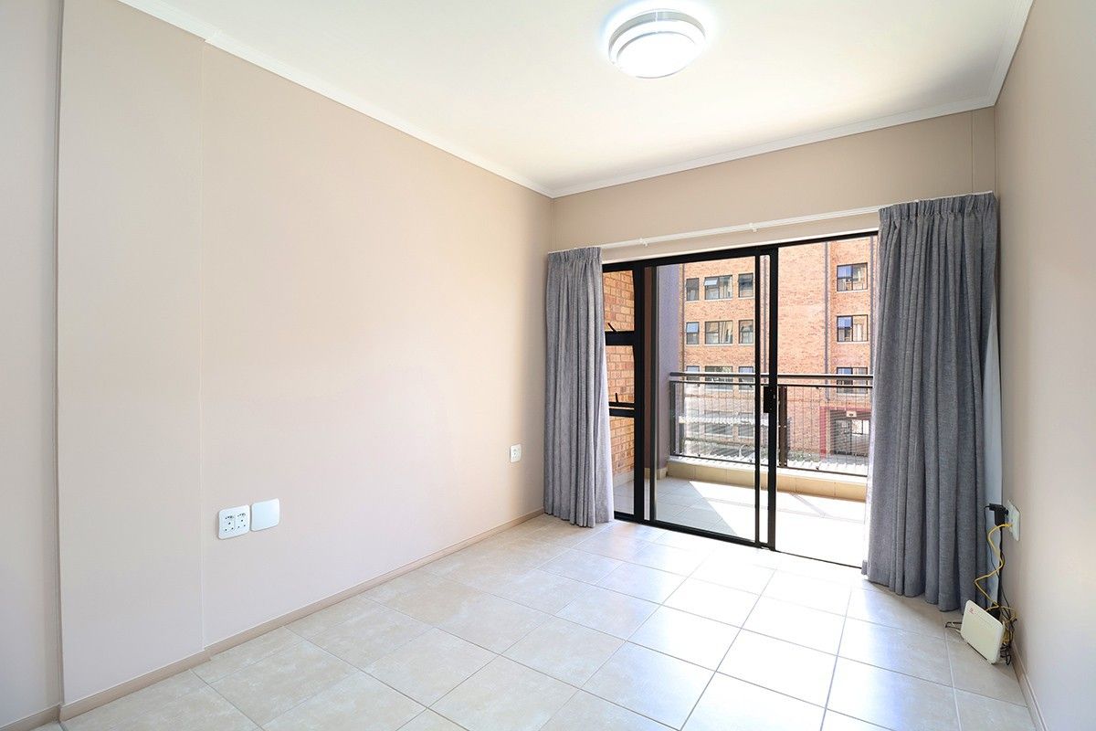 A bright, empty bedroom featuring neutral tiled flooring, a ceiling light fixture, and a sliding glass door providing direct access to a private balcony.