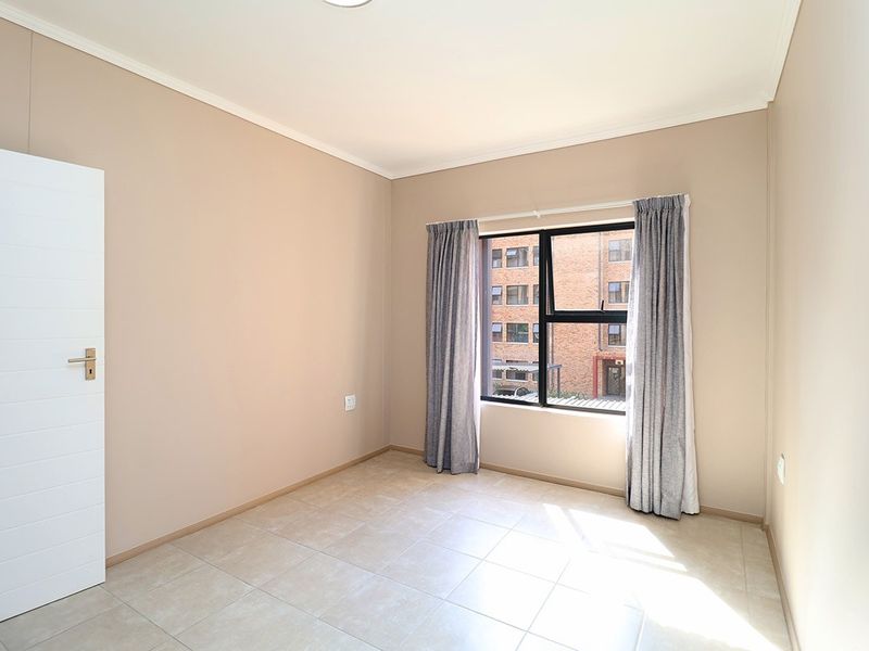 A bright, empty bedroom featuring neutral wall tones, tiled flooring, and a large aluminium-framed window with installed curtain tracks.