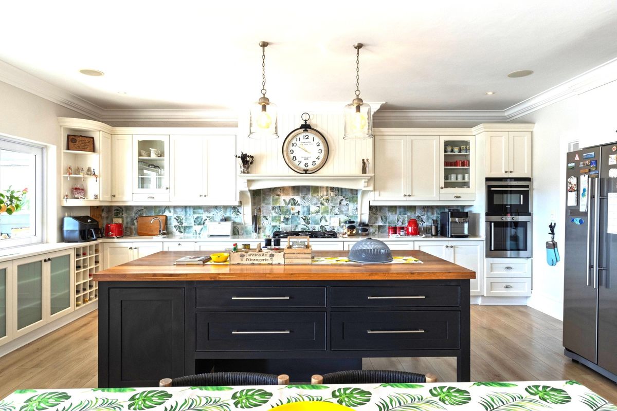 A well-appointed kitchen featuring a large central island with a wooden countertop, built-in appliances, decorative tiled backsplash, and elegant pendant lighting.