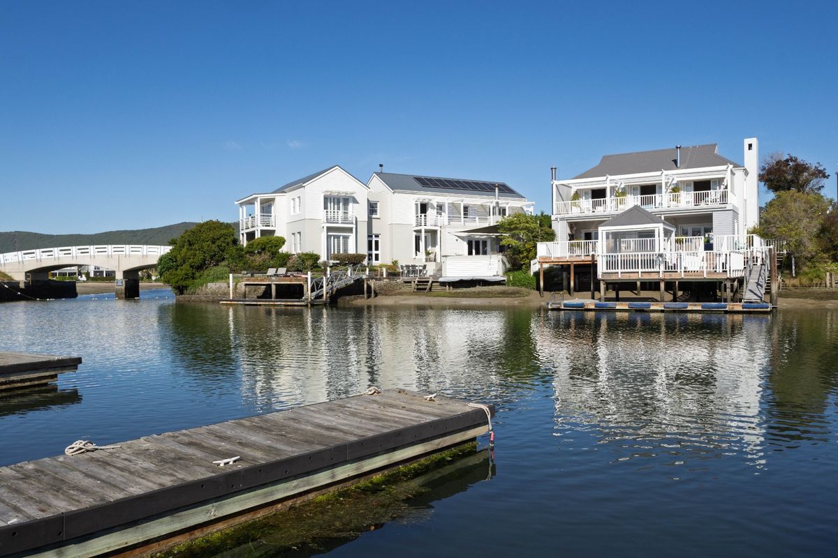 Waterfront view of residential properties featuring timber jetties, raised decks, and balconies overlooking the river with a bridge in the background.