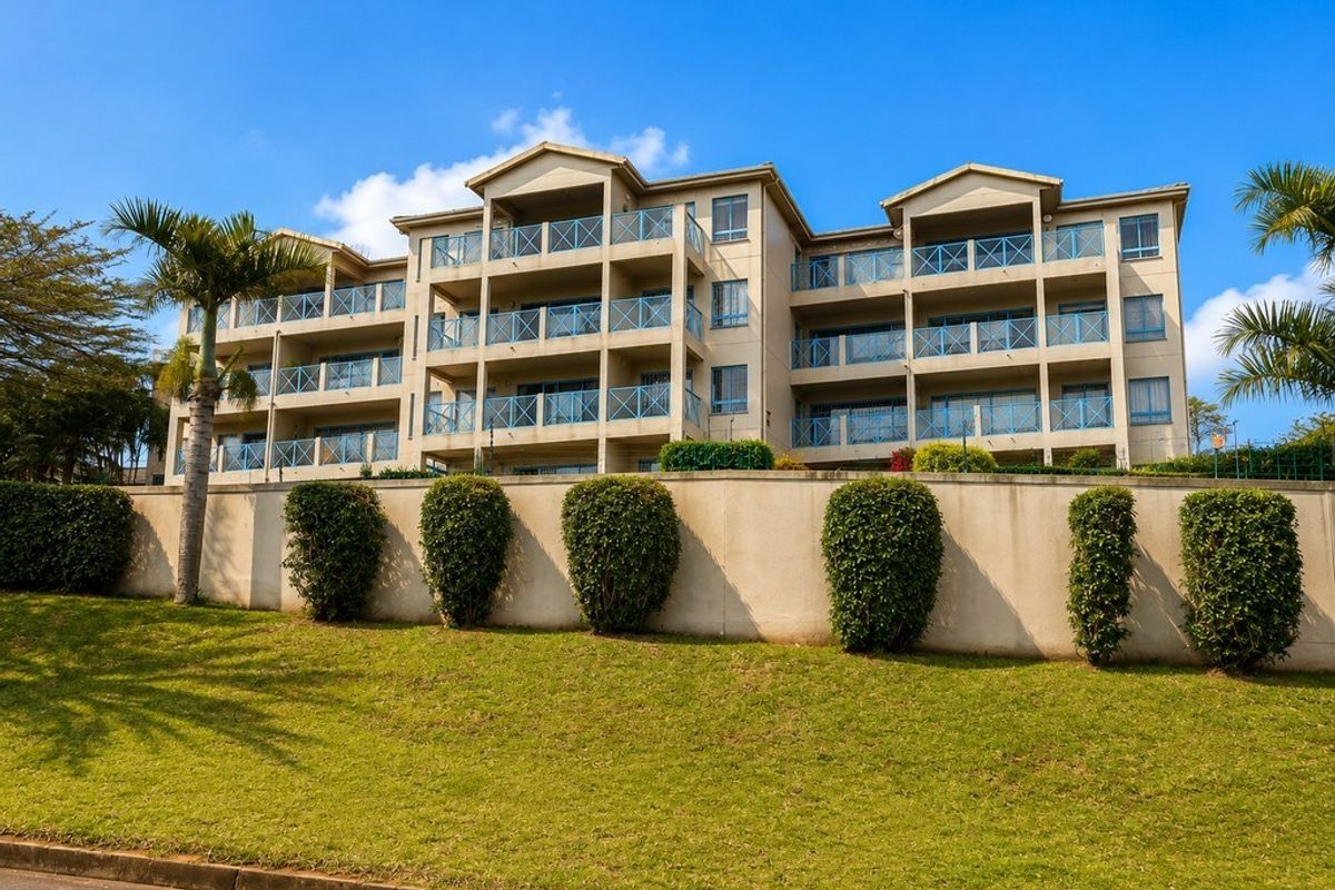 Rear view of a multi-story apartment complex featuring private balconies with glass balustrades, set above a well-maintained retaining wall and landscaped garden area.