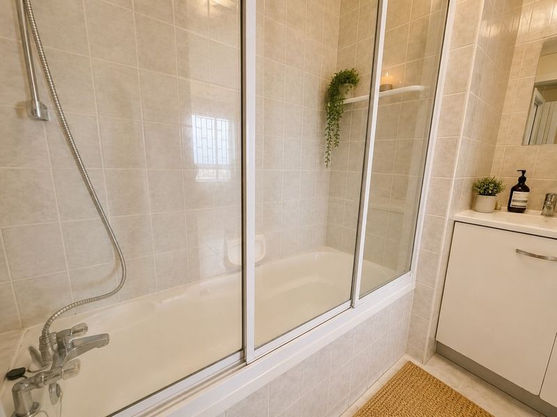 A clean, functional bathroom featuring a bathtub with a glass shower screen, tiled wall finishes, and a modern vanity cabinet with a basin.