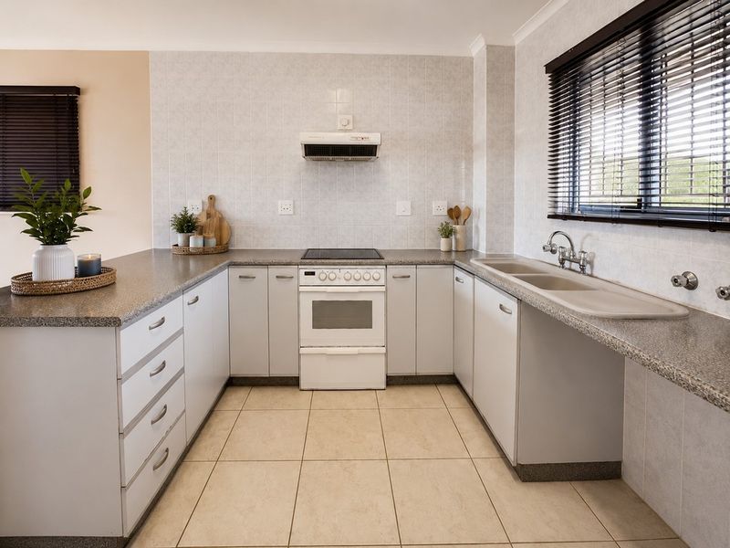 A functional U-shaped kitchen featuring light-toned cabinetry, granite-look laminate countertops, a freestanding stove with extractor, and a double basin sink.