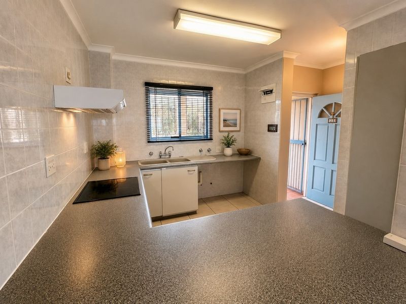 A functional kitchen featuring laminate countertops, a double bowl sink, electric cooktop, extractor fan, and tiled finishes throughout.