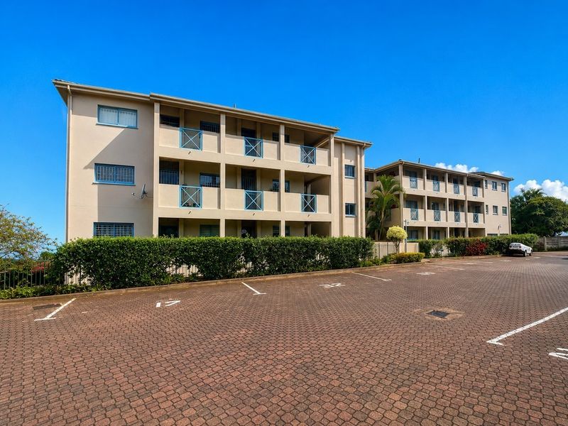 Exterior view of a multi-story apartment complex featuring paved parking, private balconies with metal balustrades, and well-maintained landscaping.
