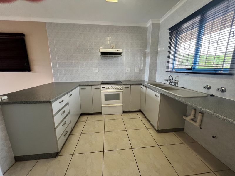 A functional kitchen featuring laminate countertops, built-in cabinetry, a freestanding stove with extractor fan, and a double sink with tiled splashback.