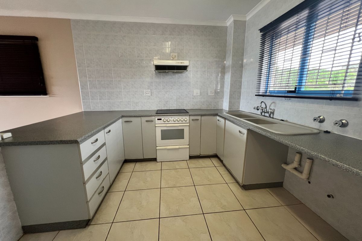 A functional kitchen featuring laminate countertops, built-in cabinetry, a freestanding stove with extractor fan, and a double sink with tiled splashback.