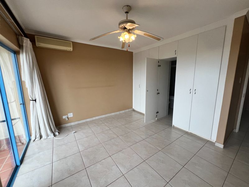 Spacious bedroom featuring tiled flooring, built-in cupboards, a ceiling fan, and an air conditioning unit, with direct access to an outdoor area.