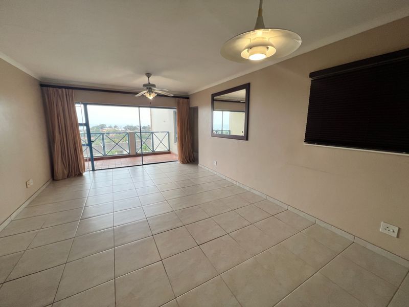Spacious, empty living area featuring neutral tiled flooring, a ceiling fan, and large sliding glass doors providing access to an outdoor balcony.