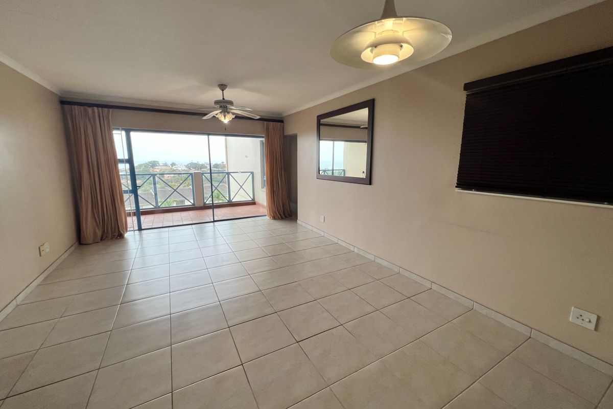 Spacious, empty living area featuring neutral tiled flooring, a ceiling fan, and large sliding glass doors providing access to an outdoor balcony.