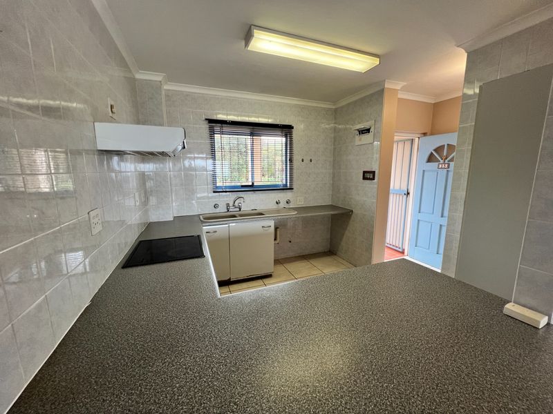 A functional kitchen featuring laminate countertops, a built-in electric hob, extractor fan, and tiled splashbacks, offering a clean and practical workspace.