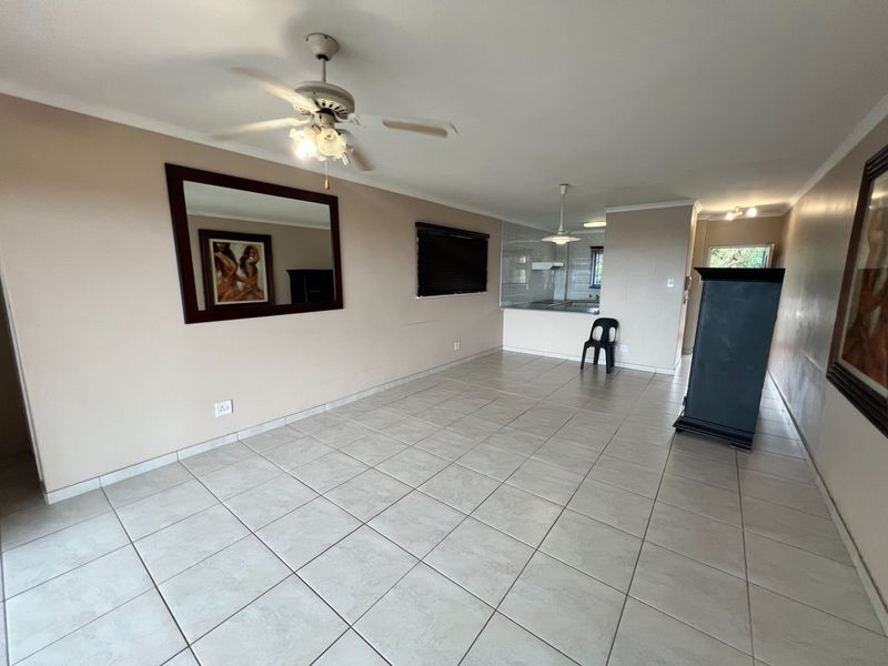 Spacious open-plan living area featuring neutral tiled flooring, a ceiling fan, and a functional kitchen layout with a breakfast bar.