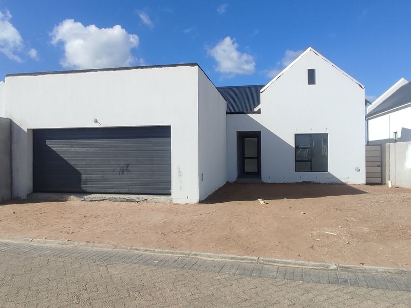 Front elevation of a modern house featuring a garage, white facade, and dark roof, currently awaiting final landscaping and garden completion.