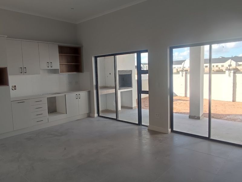 Open-plan living area featuring a kitchen with built-in cabinetry and sliding doors leading to a covered patio with a built-in braai.