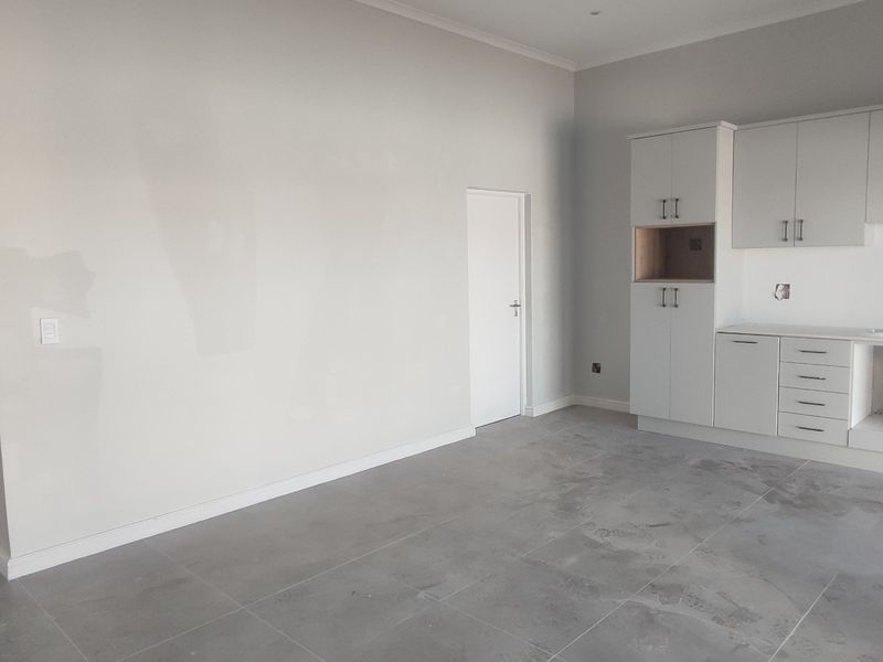 An empty, modern kitchen space featuring neutral cabinetry, tiled flooring, and a clean layout, ready for final appliance installation and personal finishing touches.