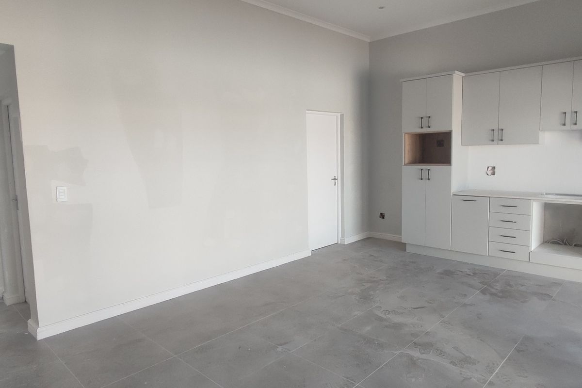 An empty, modern kitchen space featuring neutral cabinetry, tiled flooring, and a clean layout, ready for final appliance installation and personal finishing touches.