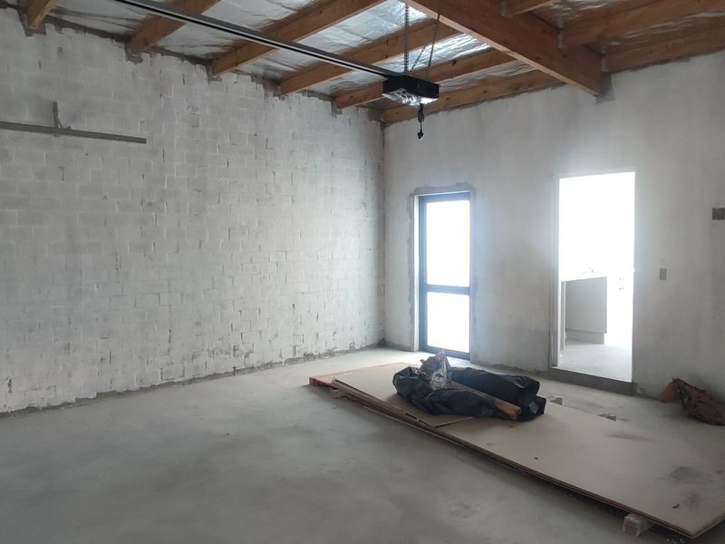 An unfinished garage space featuring exposed timber roof trusses, concrete flooring, and painted brick walls, offering a blank canvas for storage or workshop use.