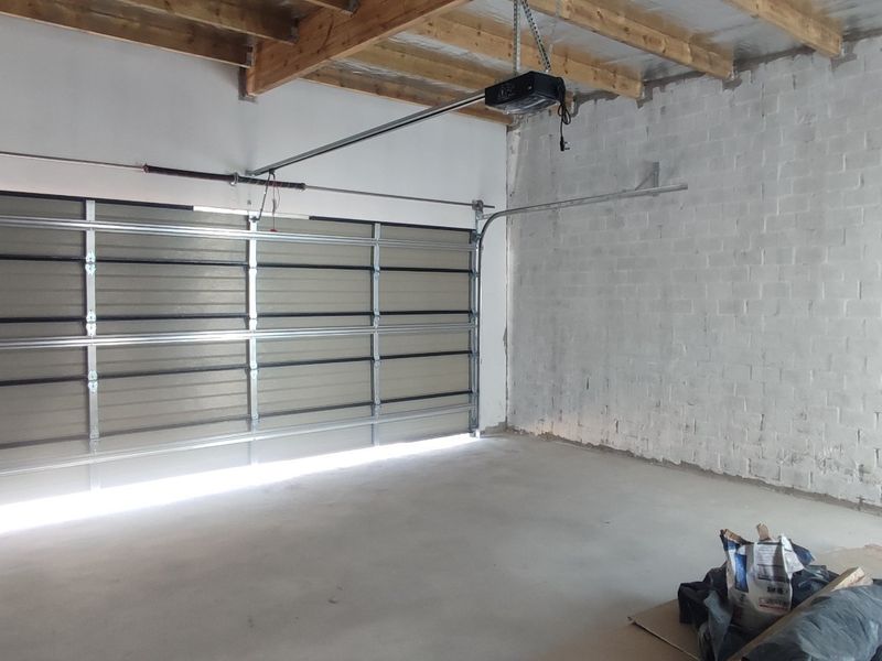 A spacious, unfinished garage featuring a sectional door, exposed timber roof trusses, and concrete flooring, offering a blank canvas for storage or workshop use.