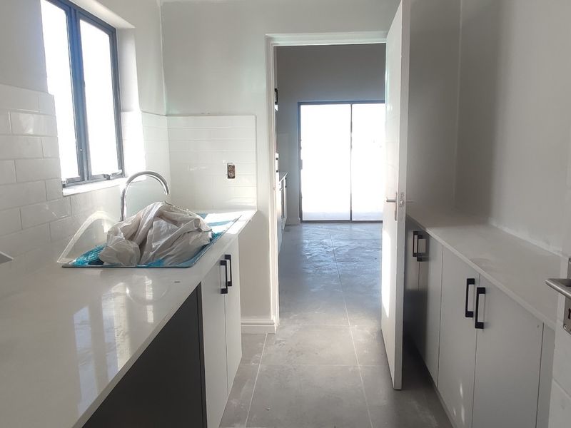 A modern, newly finished scullery featuring quartz countertops, subway tile backsplash, and ample built-in cabinetry, currently awaiting final electrical finishing.