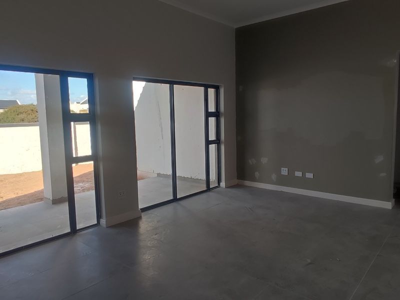 An empty, open-plan living area featuring large sliding glass doors leading to an outdoor patio, with neutral tiled flooring and unfinished wall surfaces.