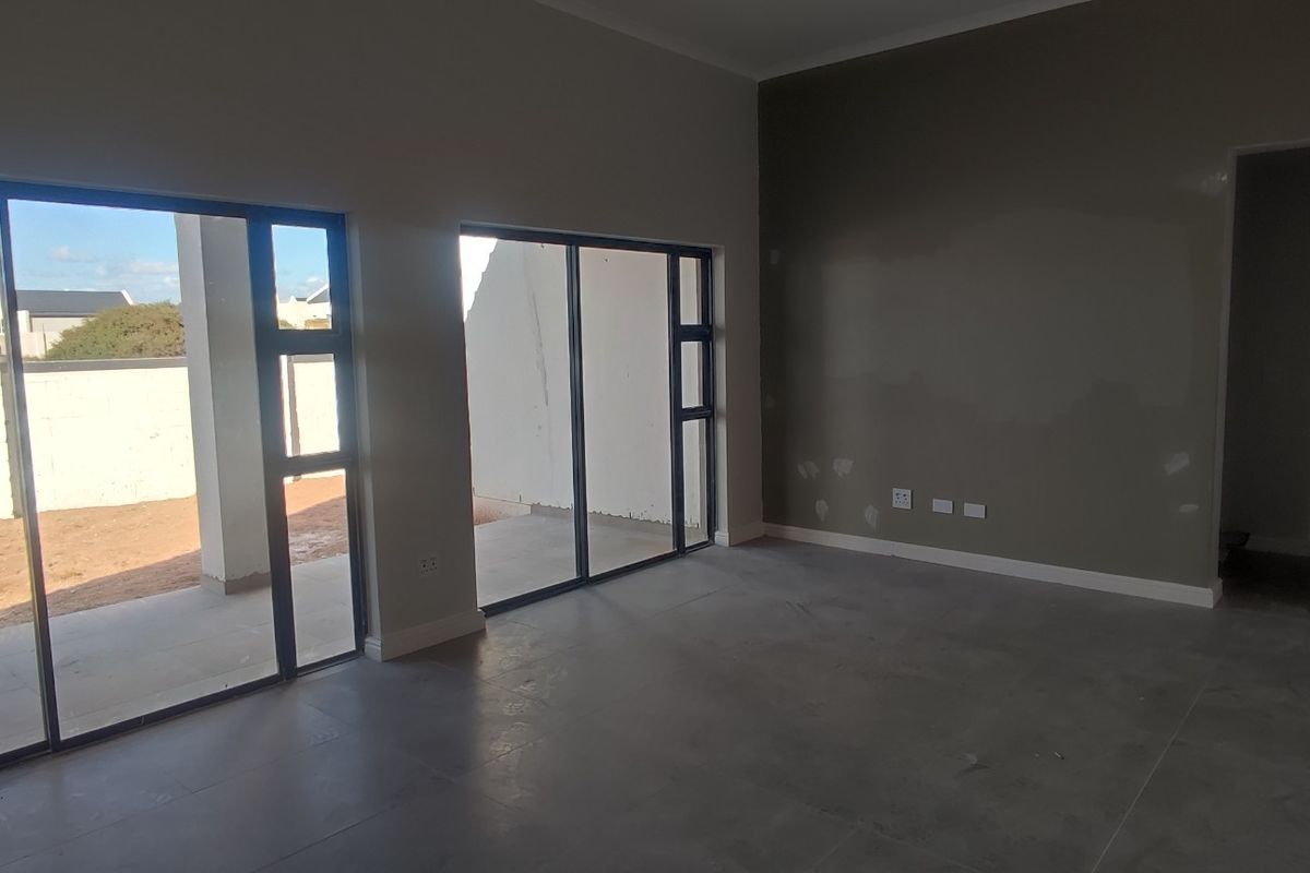 An empty, open-plan living area featuring large sliding glass doors leading to an outdoor patio, with neutral tiled flooring and unfinished wall surfaces.