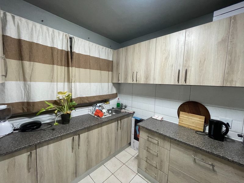 A functional kitchen featuring light wood-look cabinetry, granite-effect countertops, a stainless steel sink, and neutral tiled flooring with a tiled backsplash.
