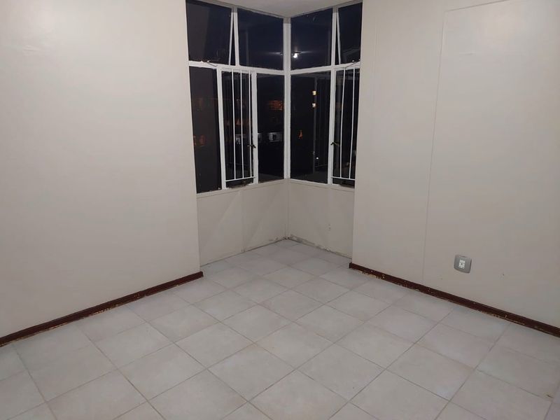 An empty bedroom featuring tiled flooring, a corner window with security bars, and neutral wall finishes.