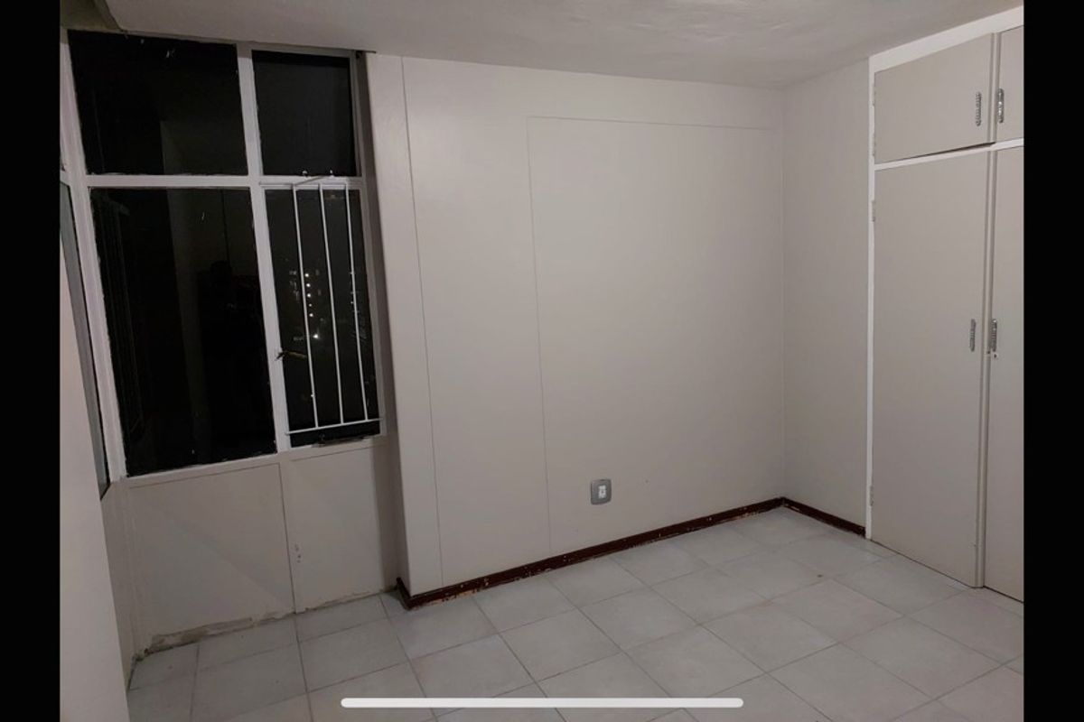 An empty bedroom featuring tiled flooring, a built-in wardrobe, and a window with security bars.
