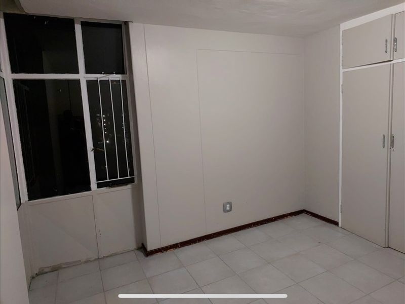 An empty bedroom featuring tiled flooring, a built-in wardrobe, and a window with security bars.