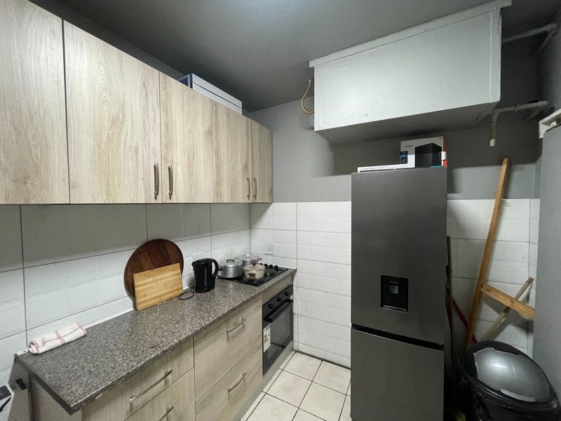 Compact kitchen featuring light wood-finish cabinetry, granite-look countertops, tiled backsplash, and integrated oven and hob.