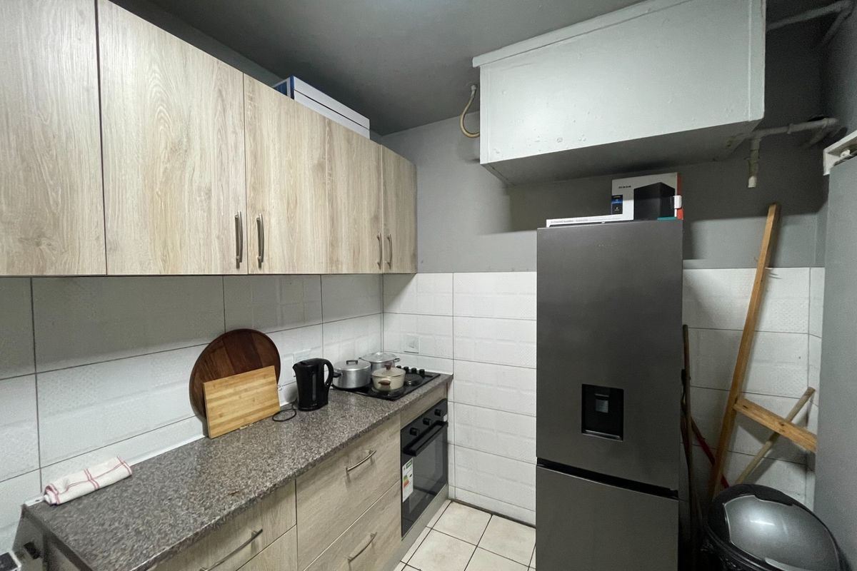 Compact kitchen featuring light wood-finish cabinetry, granite-look countertops, tiled backsplash, and integrated oven and hob.