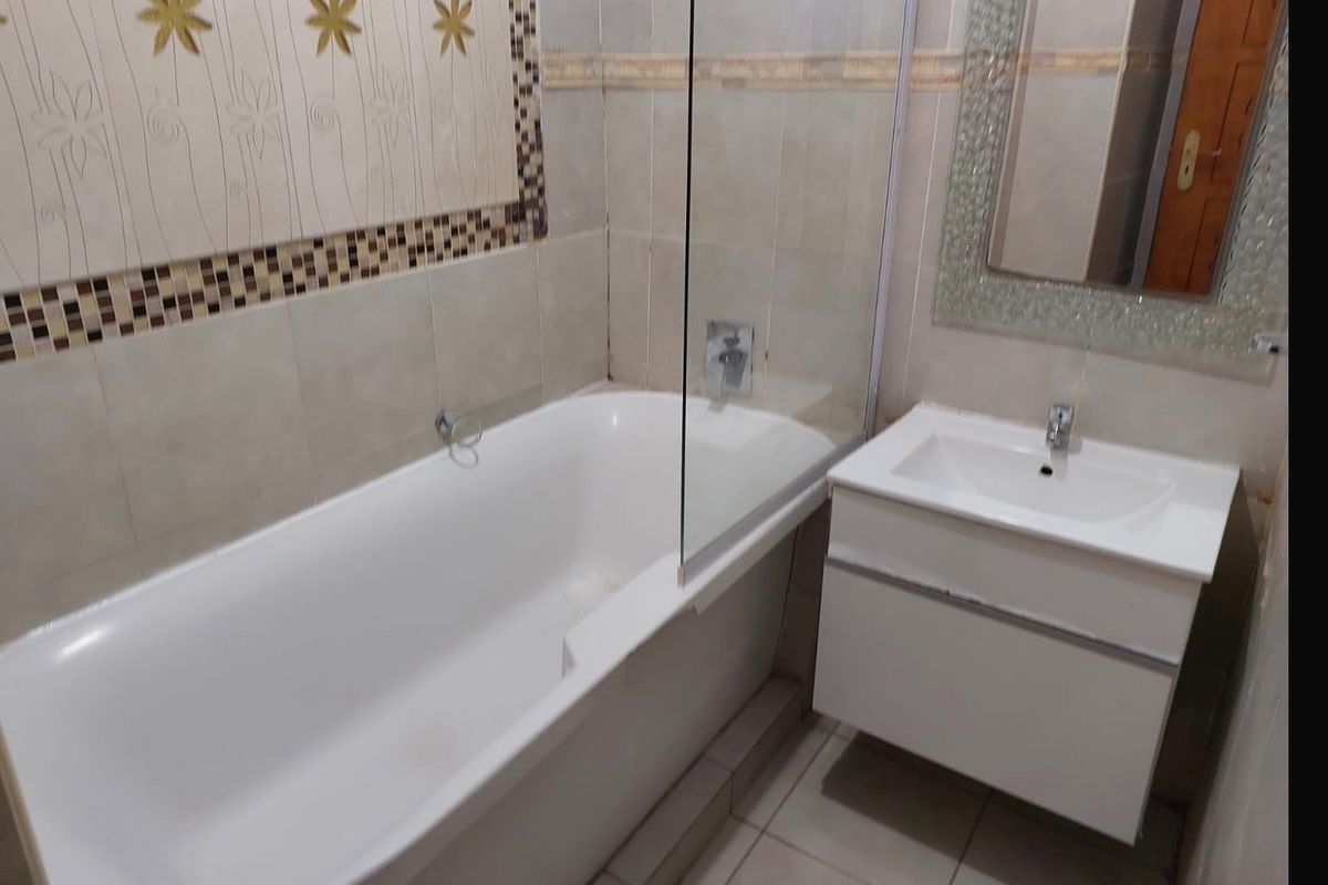 A functional bathroom featuring a bathtub with a glass shower screen, a wall-mounted vanity with a basin, and decorative tiled wall accents.