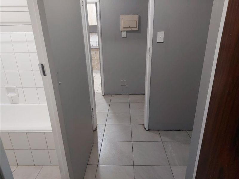A view of a tiled hallway leading to a bathroom with a built-in bathtub, showing unfinished wall edges and missing skirting boards.